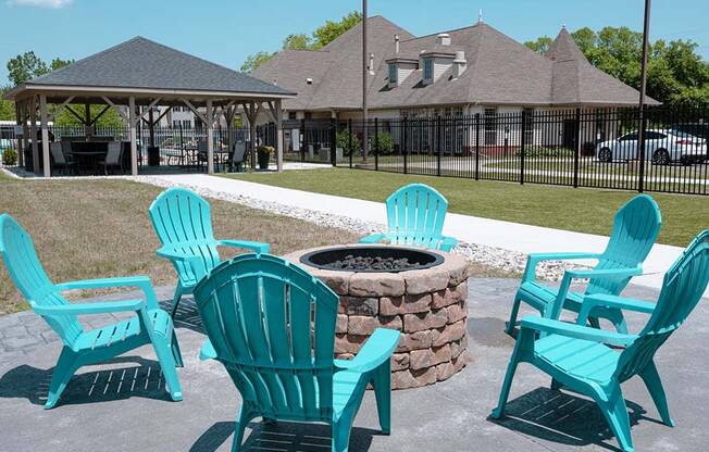 a fire pit with four blue adirondack chairs in front of a gazeb