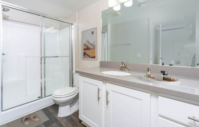A bathroom with a toilet, sink, mirror and shower.