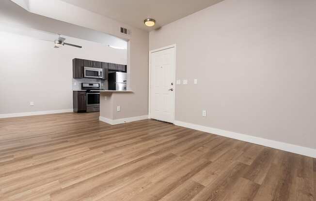 an empty living room with wood flooring and a kitchen