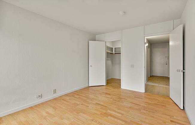 A room with white walls and wooden flooring with a door on the right.