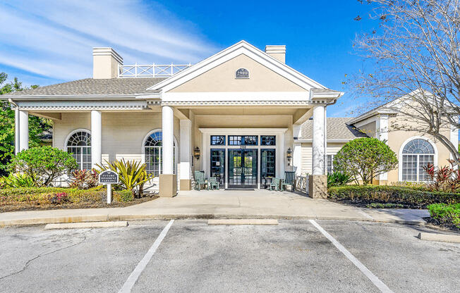 Clubhouse and leasing office exterior entryway with green rocking chairs, welcome mat, covered porch, and parking lot in front