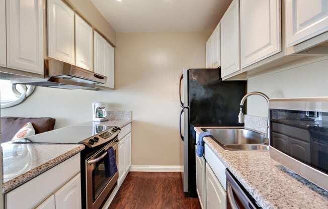 Kitchen with stainless steel electric range over range hood, refrigerator, double kitchen sink, granite countertops wood style floors