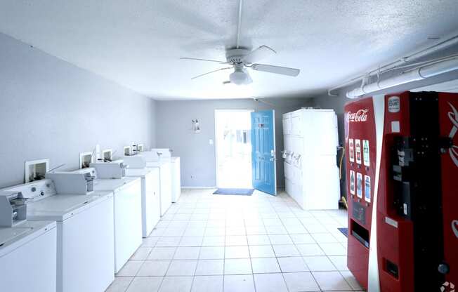 an empty laundry room with white appliances and a red coke machine