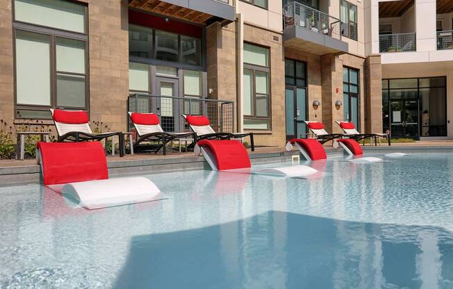 a pool with red lounge chairs and a building in the background