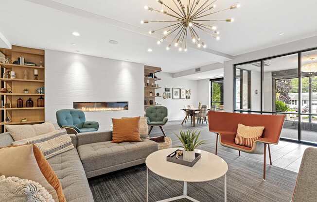 A living room with a grey sofa, a green armchair, a brown armchair, a white coffee table, a fireplace, and a chandelier.