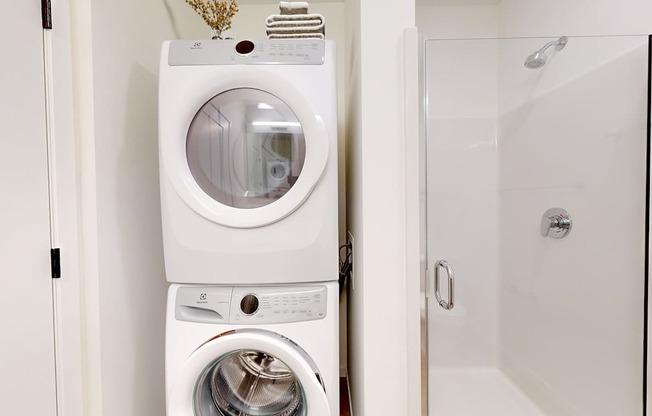 A white washing machine and dryer stacked on top of each other in a small laundry room.