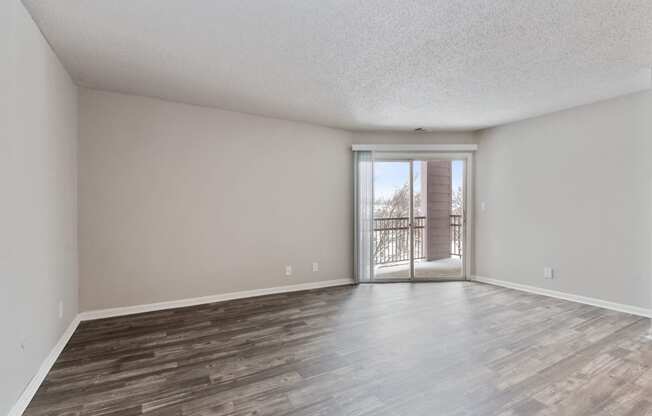 an empty living room with a sliding glass door to a balcony at Eastwood Crossings, Kansas City, MO, 64129