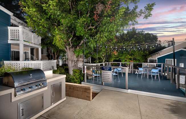 A patio with a grill and chairs is surrounded by trees.