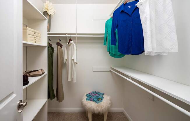 A white closet with clothes hanging and a stool in front.