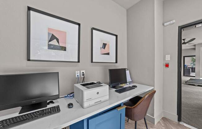 A modern office with a desk, two monitors, a laptop, and two framed pictures on the wall.