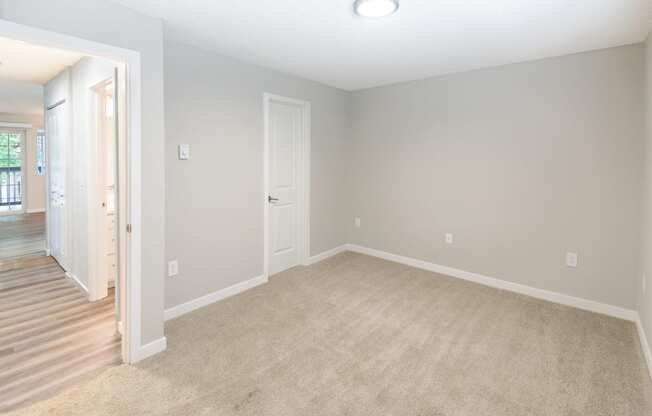 an empty living room with carpet and a door to a hallway