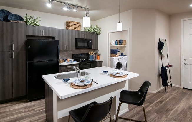 a kitchen with a large white island with two chairs in front of it and a black refrigerator