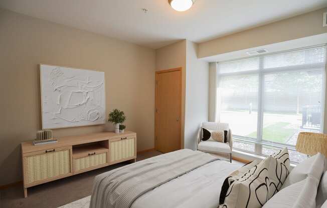 a bedroom with a large window and a bed with a white comforter