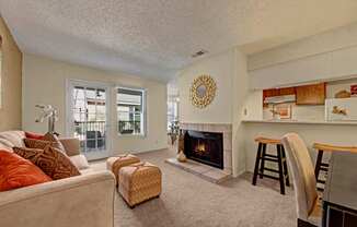A warm, inviting living room here at Cypress Pointe with soft beige carpet, neutral walls, and a cozy fireplace serving as a central feature. An open layout connects to the kitchen with a breakfast bar and seating, while glass doors bring in natural light and provide access to a private patio.