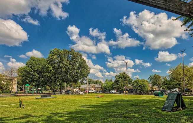 A park with a green grass field and a person playing.