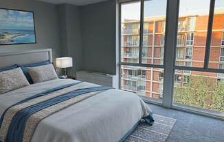 A bedroom with a large bed and a view of a building outside the window.
