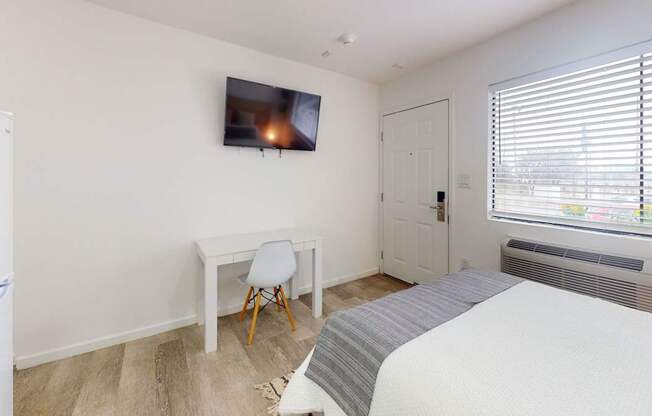A bedroom with a bed, desk, chair, and a television mounted on the wall.