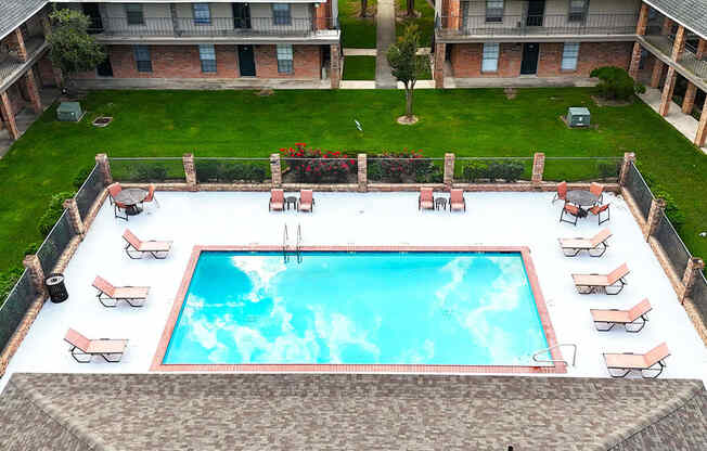 A swimming pool surrounded by lounge chairs and a brick building.