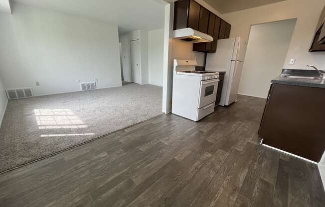 an empty living room with a kitchen in the background