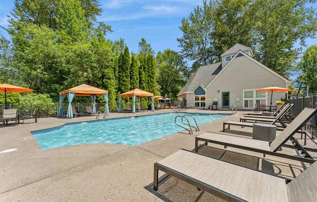 A pool area with sun loungers and a building in the background.