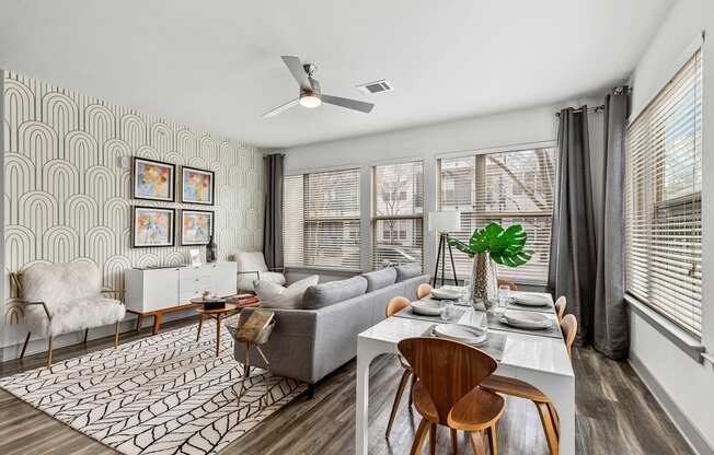 A modern living room with a grey couch, a white dining table, and a patterned rug.