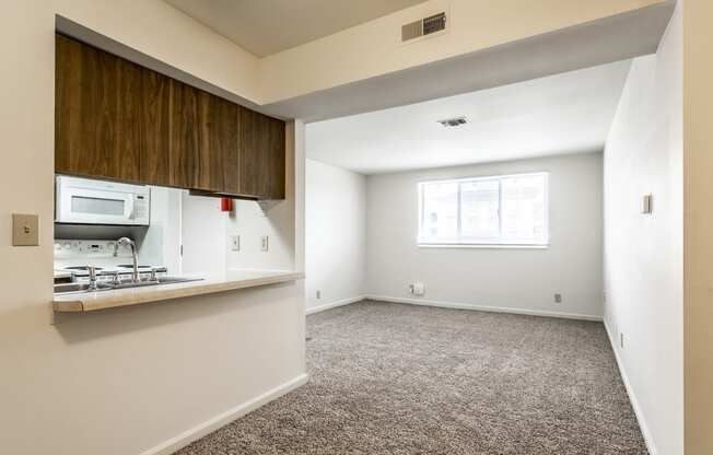 an empty living room with a kitchen and a window