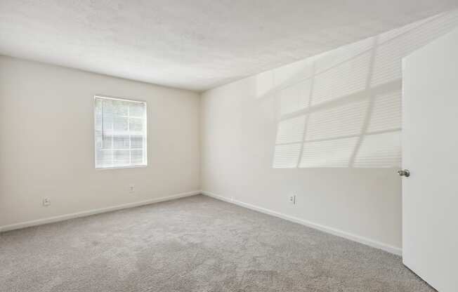 an empty bedroom with white walls and carpet and a window