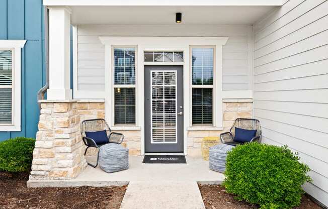 the front porch of a home with two chairs and a door