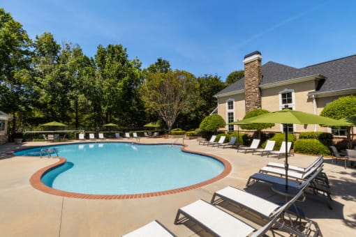 a swimming pool with chairs and umbrellas in front of a house