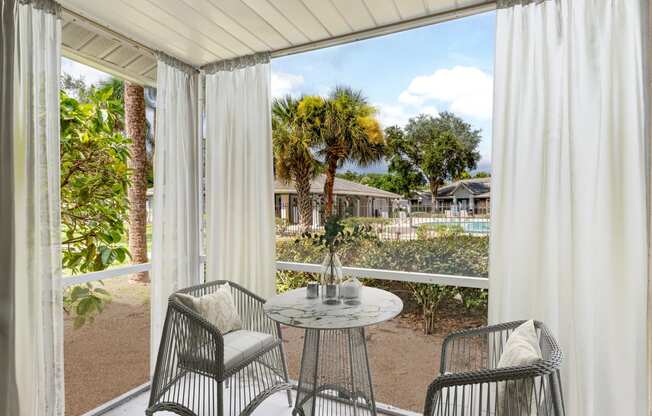 a patio with white curtains and a table and chairs at Aqua Bay Apartments in Naples, FL 34116
