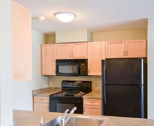 View of well equipped kitchen with black appliances, wood cabinetry, and breakfast bar