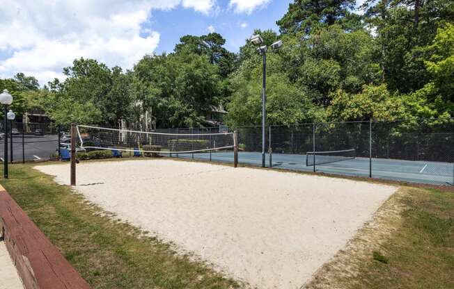 the sand volleyball court is in front of the tennis court and trees