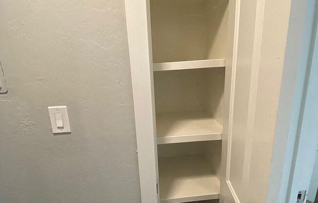 A white closet with shelves and a light switch on the wall.