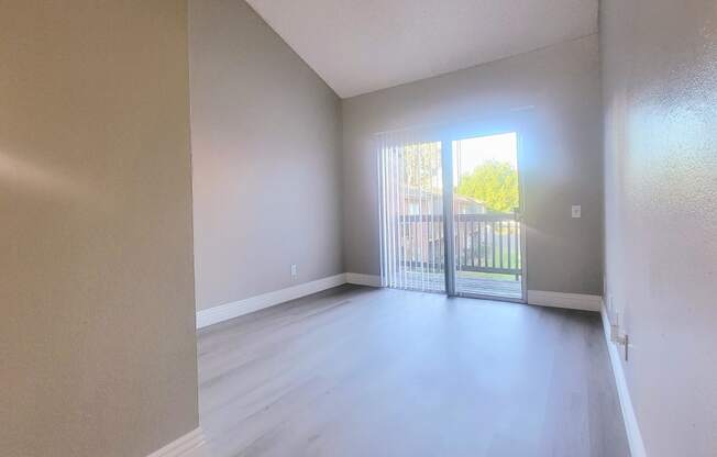 an empty living room with a sliding glass door to a balcony