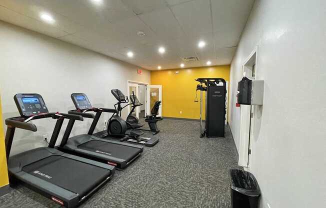 A gym with treadmills, elliptical machines, and a weight rack.