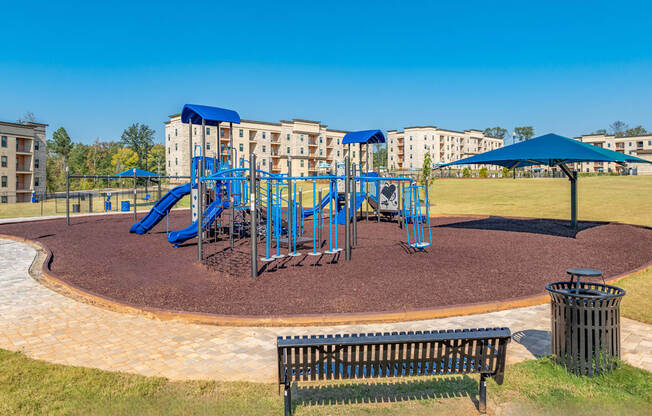 a playground with blue playset and umbrellas in front of apartments