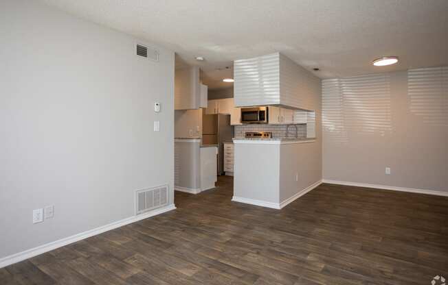 an empty living room with a kitchen in the background