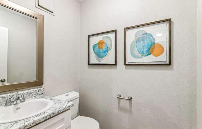 A bathroom with a toilet, sink, and two framed artworks on the wall.