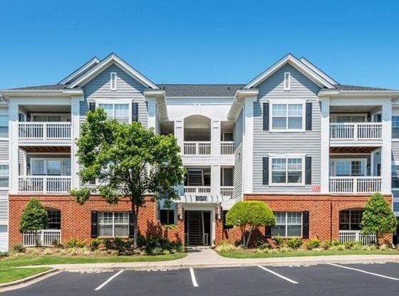 A large apartment complex with multiple balconies and a parking lot in front.