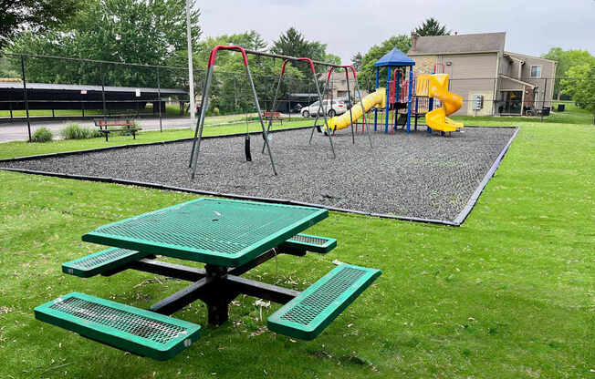 A playground with a green picnic table and a yellow slide.