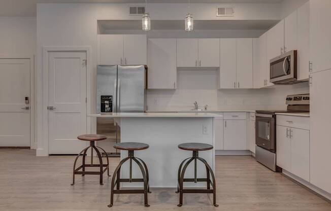 A kitchen with white cabinets and a white island with two stools in front.