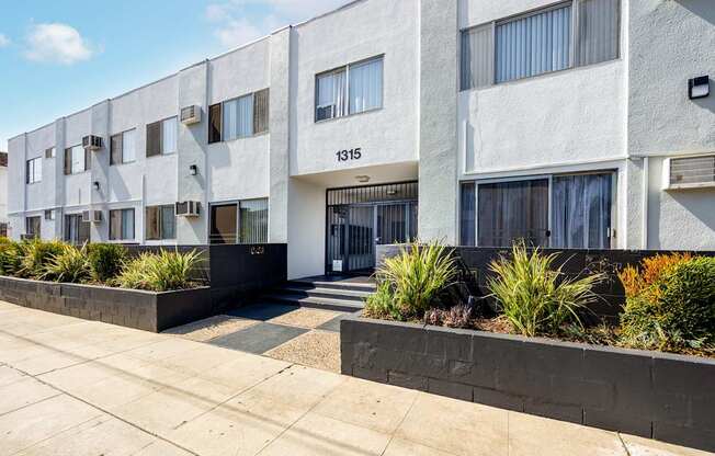 an apartment building with a sidewalk and plants in front of it