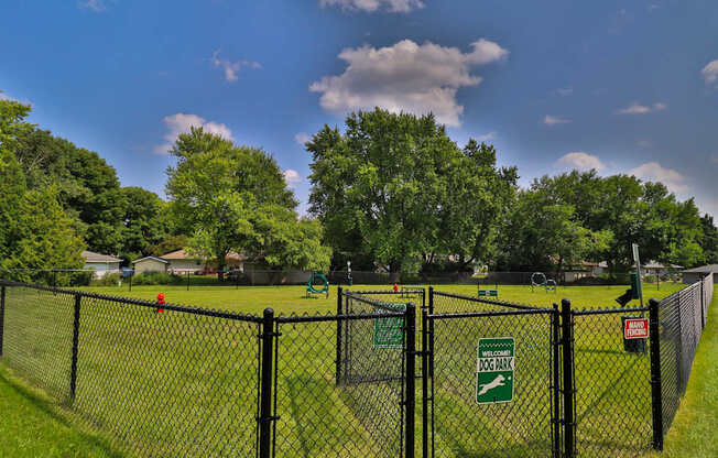 A black fence with a green sign that says Dog Park.