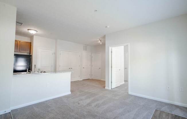 A spacious living room with a kitchen area to the left and a doorway leading to another room.