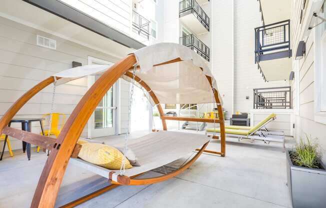 a hammock chair with a yellow pillow sits on a patio in front of a white building