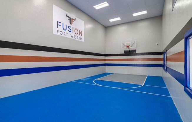 indoor basketball and racquetball court at fusion Fort Worth apartments with blue floor and apartment logo on the wall