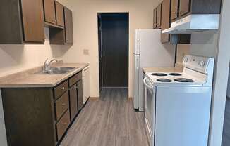 a kitchen with a stove refrigerator and a sink with wood style flooring