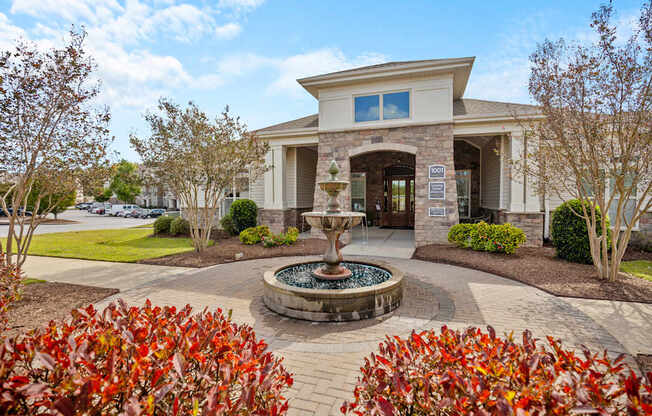 A building with a fountain in front of it surrounded by red bushes.