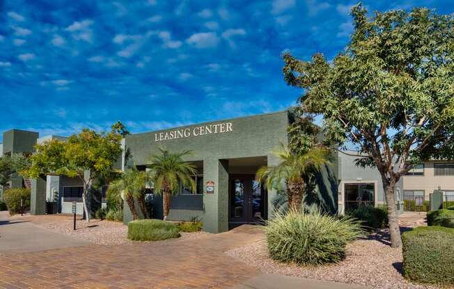 The leasing center is surrounded by greenery and has a clear blue sky above.