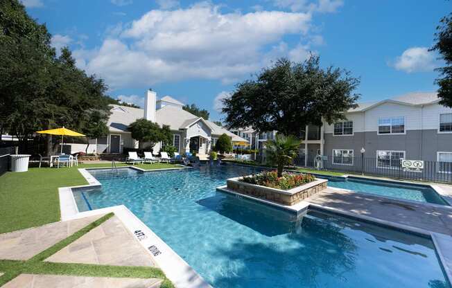 A large swimming pool with a small waterfall and a hot tub.